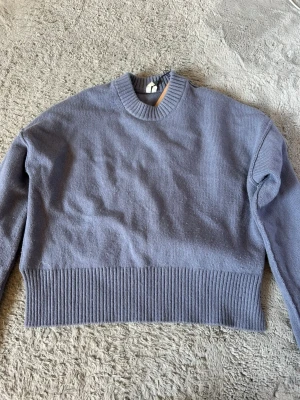 Ljuslila cropped stickad tröja från Arket  - Trendig ljuslila stickad tröja med croppad passform och bred ribbad kant nedtill. Tröjan har rund halsringning och långa ärmar. Perfekt för lager på lager och enkel att styla till jeans eller kjol.