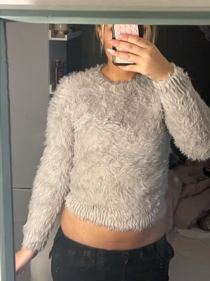 Ljusgrå fluffig stickad tröja - Supermjuk och fluffig stickad tröja i ljusgrå färg. Tröjan har rund halsringning och långa ärmar, perfekt för att hålla sig varm. Materialet är syntetiskt med en shaggy look som känns riktigt cozy och trendigt.🥰