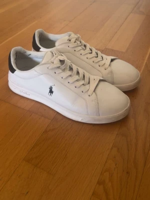 Vita Polo Ralph Lauren sneakers - Snygga vita sneakers från Polo Ralph Lauren med klassisk låg profil. Skorna har svart detalj vid hälen och den ikoniska Polo-loggan på sidan. Priset går att diskutera 