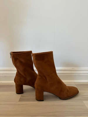 Bruna stövletter i mocka med klack - Snygga bruna stövletter i mjuk mocka med fyrkantig tå och bred klack. Dragkedja baktill för enkel påtagning. Perfekta till höstens outfits och ger en trendig touch till din stil.