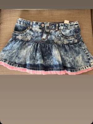 Jeanskjol med rosa volangkant - Snygg kort jeanskjol i ljusblå färg! Köpt från en vintage butik i Stockholm så den är limited edition. As snygg model och färg! Är lite osäker på storlek men skulle säga  M/ W28. Helt ny aldrig använd men inga prislappar fanns när jag köpte den!