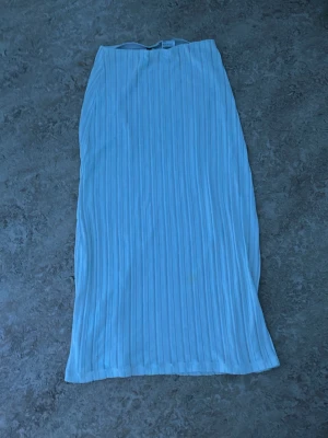 Vit långkjol med ribbade ränder - Säljer en vit långkjol med ribbade vertikala ränder. Kjolen har en luftig och lätt struktur som ger en snygg siluett. Perfekt för dig som gillar stilrena plagg med lite extra detalj. Passar till många olika looks!