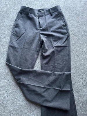 Grå kostymbyxor  - Snygga grå kostymbyxor från Gina Tricot med utsvängda ben. Perfekta för en clean och trendig outfit. Aldrig använda!