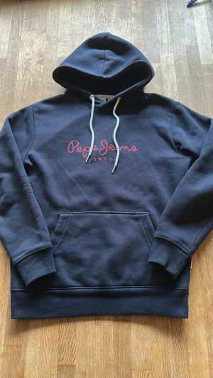 Marinblå hoodie från Pepe Jeans - Snygg marinblå hoodie från Pepe Jeans med röd broderad logga på bröstet och texten 'London' under.  Xs men sitter som S, mått finns
