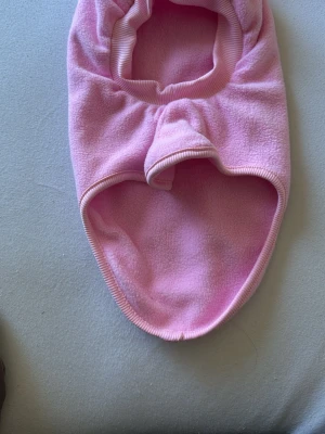 Rosa fleecebalaklava - Säljer en mjuk och varm balaklava i ljusrosa fleece. Balaklavan har en öppning för ansiktet och täcker både huvud och hals, perfekt för kalla dagar. Materialet är stretchigt och känns skönt mot huden. Enkel och stilren design utan synligt märke.