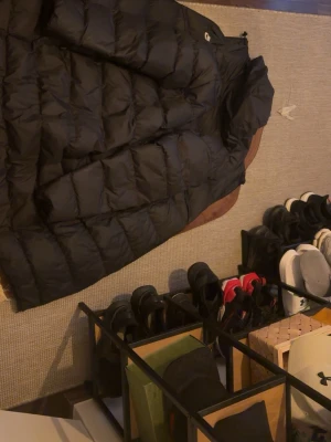 Svart lång dunjacka från Nike - Säljer en svart lång dunjacka från Nike med huva och dragkedja framtill. Jackan har en puffig design och är perfekt för kalla dagar. Klassisk Nike-logga på bröstet och praktiska fickor på sidorna. Passar dig som vill ha både stil och värme.