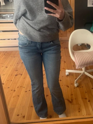 Blå bootcut jeans med nitar - Säljer ett par ljusblå bootcut jeans med snygga detaljer på bakfickorna, som veck och silvriga nitar. Jeansen har klassisk femficksmodell och är tillverkade i denim med lite stretch för skön passform. Perfekta för dig som gillar en avslappnad men trendig stil💕💕