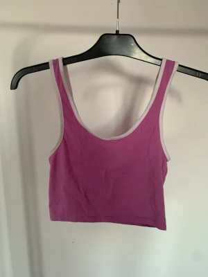 Ljuslila croppad linnetopp Monki - Säljer en ljuslila croppad linnetopp från Monki. Toppen är ärmlös med vita kanter och har en enkel, sportig look. Perfekt att matcha med höga jeans eller kjol för en chill stil.