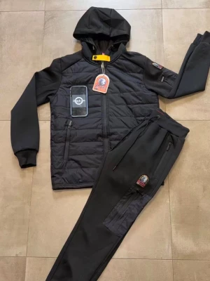 Svart loungewear set med huva - Snyggt svart loungewear set från Parajumpers med quiltad huvtröja och matchande byxor. Tröjan har dragkedja, huva och patchdetaljer på bröstet och ärmen. Byxorna har resår i midjan, fickor med dragkedja och en patch på benet. Perfekt för chill dagar hemma.