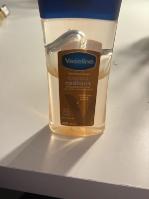 Vaseline Cocoa Radiant Body Oil 200ml - Vaseline Intensive Care Cocoa Radiant är en kroppsolja med 100% ren kakaosmör som ger huden lyster och återfuktning. Oljan kommer i en genomskinlig plastflaska med blått lock och rymmer 200 ml. Perfekt för dig som vill ha mjuk och glowig hud.