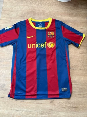 FC Barcelona Messi matchtröja 2012 - Säljer en klassisk FC Barcelona matchtröja från Nike med Messi och nummer 10 på ryggen. Tröjan har blå och röda vertikala ränder, gula detaljer vid krage och ärmslut samt tryckta loggor för Nike, Barcelona och Unicef. Tillverkad i lätt, ventilerande material. Helt äkta köpt på camp nou