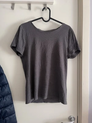 Mörkgrå basic t-shirt - En enkel mörkgrå t-shirt med rund hals och korta ärmar. Tillverkad i mjukt bomullsmaterial och har en klassisk passform som funkar till det mesta. Perfekt för en avslappnad och stilren look.