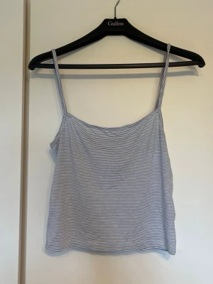 Randig ljusblå linnetopp - Säljer en enkel och snygg randig linnetopp med tunna axelband. Toppen är ljusblå och vit med smala horisontella ränder och har en rak, croppad passform. Perfekt för varma dagar och lätt att matcha med jeans eller shorts.