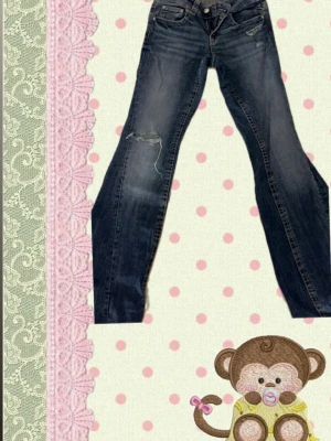 Mörkblå jeans med slitning och mönster på bakfickorna  - Snygga mörkblå jeans med slitning på ena benet och coola kontrastsömmar. Bakfickan har dekorativa sömmar och lock med knapp. Klassisk femficksmodell och rak passform. Perfekta för en avslappnad och trendig look.