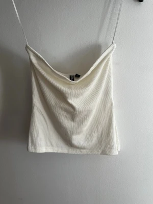 Vit ribbad tubtop - Säljer en vit ribbad tubtopp från Pieces. Toppen  har en sne med slit på ena sidan som passar perfekt till jeans eller kjol. Materialet är mjukt och stretchigt för en bekväm känsla. Lite lite krämvit