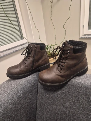Födrade Kängor, Bruna, Storlek 38 - Säljer ett par bruna stövletter med snörning och dragkedja på sidan. Skorna har en robust sula och är fodrade med svart pälsmaterial för extra värme. Perfekt för kalla dagar och snyggt till jeans eller leggings.