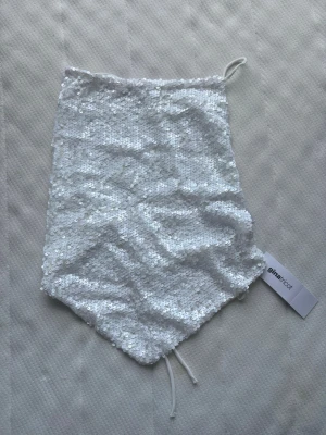 Vit paljett tubtopp från Gina Tricot - Säljer en snygg vit tubtopp från Gina Tricot, täckt med glittriga paljetter. Toppen har bandeau-modell och knytband i ryggen för justerbar passform. Perfekt för dig som vill sticka ut och glänsa lite extra.
