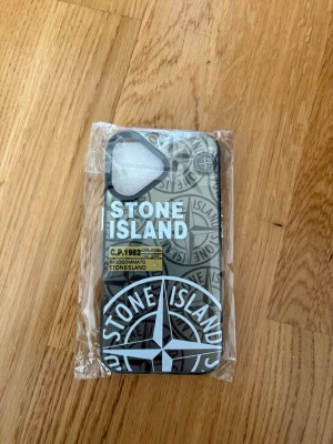 Stone Island mobilskal svart/grå - Snyggt mobilskal från Stone Island med logga och grafiskt mönster i svart och grått. Skalet har en stilren design med tydliga detaljer och passar perfekt för dig som vill ha en cool accessoar till mobilen.