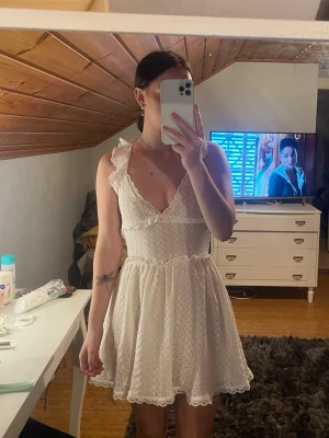 Vit spetsklänning med volangband - Söt vit klänning i spets med volangprydda axelband som korsas i ryggen. Djup urringning fram och öppen rygg ger en somrig känsla. Kjolen är lätt utsvängd och klänningen har fina spetsdetaljer över hela tyget. Klor på shien för ca 200kr, bara provat den på.