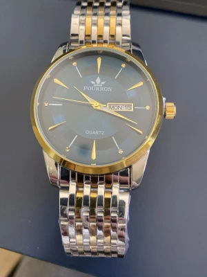 Blå och guld herrklocka Quartz  - Stilren herrklocka från Fourron med blå urtavla, guldfärgade detaljer och dag/datumvisning. Armbandet är i silver och guldtonat metall, vilket ger en lyxig känsla. Perfekt accessoar för dig som vill sticka ut med en elegant look.                     Den är sprillans ny. Kommer i orginalförpackning