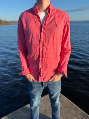 Rosa linneskjorta från Ralph Lauren - Säljer en snygg rosa skjorta från Ralph Lauren i linne. Skjortan har klassisk krage, knappar framtill och den ikoniska loggan broderad på bröstet. Perfekt för en avslappnad men stilren look. Storlek L och i extremt bra skick💪Vi säljer skjortan för endast 449kr men kan absolut gå ner i pris vid snabb och smidig affär🥰Långärmad modell med normal passform.