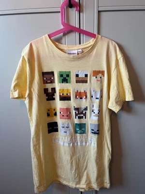 Gul Minecraft t-shirt med tryck - Gul t-shirt från Minecraft med färgglatt tryck av olika karaktärer från spelet på framsidan. Klassisk rund hals och korta ärmar. Tillverkad i mjuk bomull som är skön att ha på sig. Perfekt för dig som gillar gaming och vill ha en unik stil.