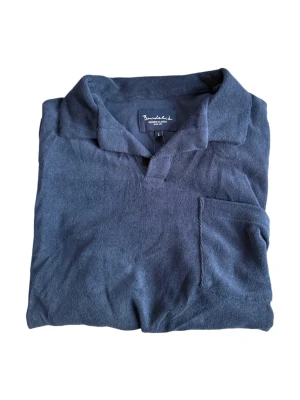 Mörkblå frottéskjorta Bondelid - Mjuk och avslappnad mörkblå skjorta från Bondelid i frotté. Skjortan har korta ärmar, öppen krage och en bröstficka för chill vibe. Perfekt till sommaren när du vill vara både bekväm och snygg.