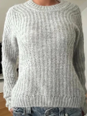 Ljusgrå stickad tröja i mohairmix - Mysig ljusgrå stickad tröja med rund hals och ribbade muddar. Tröjan har en luftig, fluffig struktur och är gjord i en mjuk mohairmix. Perfekt för lager på lager och ger en avslappnad men ändå stilren look.
