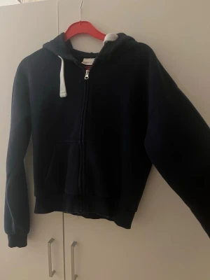 Mörkblå zip hoodie med huva - mörkblå hoodie med dragkedja och stor ficka framtill. Hoodien har bra passform och ribbade muddar vid ärmar och nederkant. 
