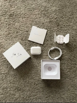 Apple AirPods Pro med laddningsetui - Säljer ett par Apple AirPods Pro med trådlöst laddningsetui. Hörlurarna är vita och har en stilren, kompakt design i plast. Medföljer originalkartong, laddningskabel, extra silikonpluggar och manual. Perfekta för dig som vill ha grymt ljud och brusreducering.