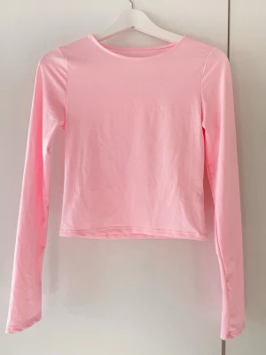 Ljusrosa långärmad topp - Säljer en ljusrosa långärmad topp i mjukt och stretchigt material. Tillverkad av 95% polyester och 5% elastan, vilket gör den bekväm och följsam. Enkel och stilren design med rund halsringning. Perfekt att matcha med jeans eller kjol.