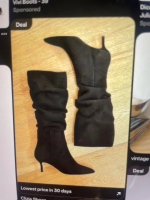 Svarta slouchy stövlar med klack - Snygga svarta stövlar med slouchy skaft och spetsig tå. De har en smal klack och är tillverkade i mockaimitation. Perfekta för att lyfta vilken outfit som helst och ger en trendig vibe.