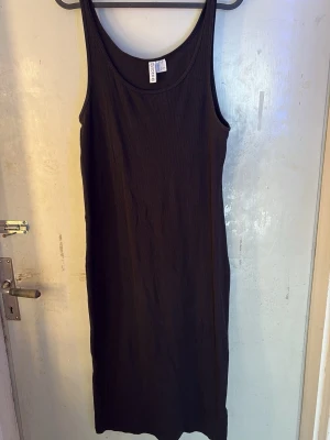 Svart ribbad långklänning  - En svart ribbad långklänning  med rund halsringning och ärmlös design. Klänningen har en enkel och stilren look som passar perfekt till sommaren. Materialet är mjukt och stretchigt för en bekväm passform. Perfekt sommarklänning