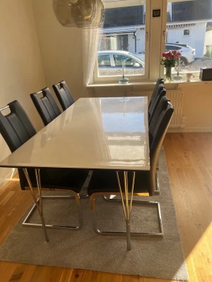 Matbord med sex svarta stolar - Säljer ett modernt matbord med vit, blank rektangulär bordsskiva och kromade metallben. Till bordet hör sex svarta stolar i konstläder med kromade ben och stilren design. Perfekt för dig som gillar minimalistisk inredning.