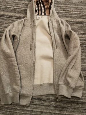  Burberry grå zip up hoddie  - Grå Burberry zip up hoddie med fina mönster i luvan.priset kan diskuteras.Litten i storlek passar bäst M