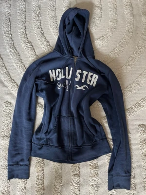 Marinblå vintage Hollister hoodie - Hej nu säljer jag en söt vintage Hollister hoodie med ett fint tryck på framsida. Dessa är väl eftertraktade på secondhand marknaden!