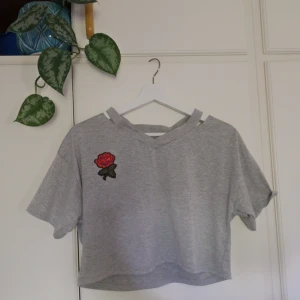 Croppad Grå Tgshirt med Ros Patch🥀 - Snygg croppad TShirt otroligt lite använd. Broderas ros över bröstet. 🥀Fint skick! Den har liksom "avklippt" krage över axlarna. Storlek S, säljes pga lite liten på mig! 