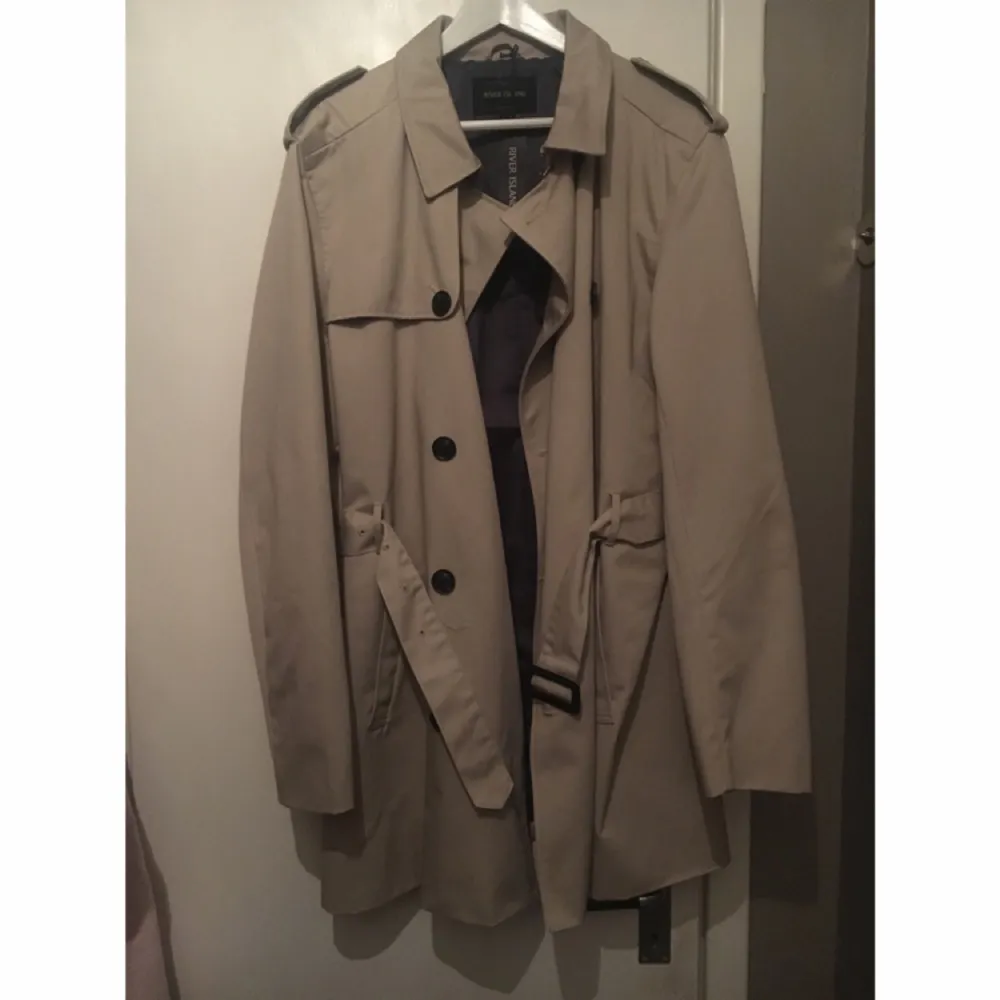 Trench coat i storlek L från River Island. Den är väldigt stor i storleken så att en XL kan bära denna utan problem. Den är aldrig använd och lapparna sitter kvar.  Jackan är köpt i London för £75 (pund) = ca 890kr. Jackor.