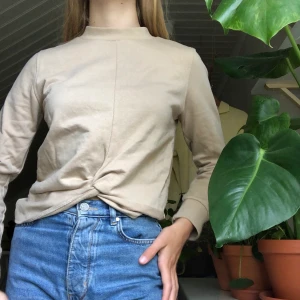 En beige sweatshirt - En beige sweatshirt med knyte längs ned. Plagget är helt nära oanvänt och har storleken xs. (Köparen står för frakt).