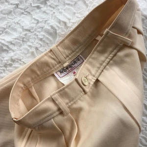 Yves Saint Laurent byxor - Ett par vrålsnygga Yves Saint Laurent vintage byxor. Jag köpte dessa begagnat och insåg sedan att de ej passade mig. Raka i modellen, klassiska kostymbyxor. Färgen är drömmigt ljusgul. Avis på den som kan ha dessa. Liten 38:a. 