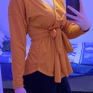 En väldigt skön och basic typ brun/orange tröja som man kan knyta om man vill ha den tajt vid midjan. Skönt material. Storlek 38 men passar 36.