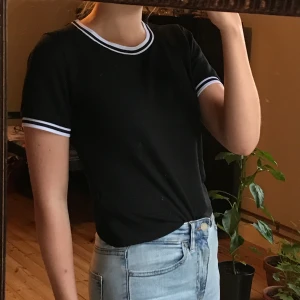 T-shirt BikBok - Svart T-shirt i lätt material med vita ränder vid båda ärmarna och vid urringningen. Köpt på BikBok. Buda! 