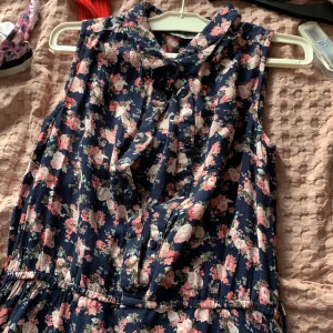 Sommar känning  - En blommig blå klänning med knappar ner till midjan, en lite krage och en lite ficka på en bröstet. 