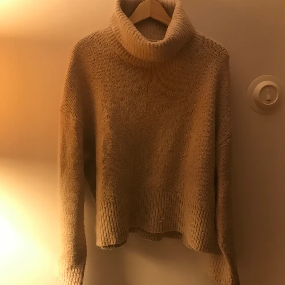 En beige stickad tröja, man ser fin ut i den, lite kortare i modellen. Stickat.