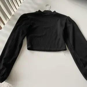 En svart tröja som är lite croppad. Hög hals. Fint mönster. Lite puffiga armar, inte för mycket. Lite ihop draget på axlarna vilket gör tröjan väldigt fin och gullig på än, ser nästan ut som lite axelvadd fast det inte är det. 