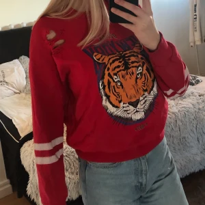 Sweatshirt från ginatricot - En fin röd sweatshirt ifrån ginatricot med tigertryck och slitningar. I mycket fint skick bortsett från de vita ränderna på armarna som är något slitna. 40kr + frakt.
