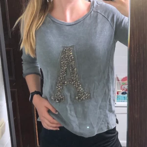 TRÖJA MED STENAR - Grå tröja med trekvartslånga ärmar & bokstaven A format av fina stenar. Köparen står för frakten💗