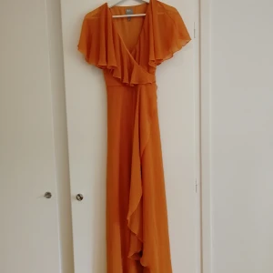 Sommar klänning  - Orange lång-klänning. Med volanger och snörning i ryggen som hjälper till att framhäva formen. Endast använd 1 gång. Väödigt bekväm