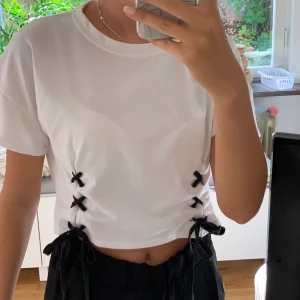 Fin vit tröja med svarta snören längst ner  - En väldigt fin vit/off white tröja som har snören längst ner som kan knytas till rosetter. Säljer då jag inte använder den. Skulle säga att den passar både s/m