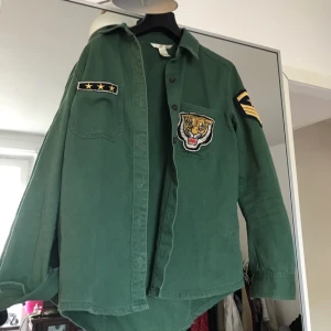  - Grön tunnare jacka som fungerar lika bra inne som ute men då på somrarna. Köpt i London. 